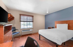 Habitación de hotel con cama, escritorio, silla, televisor y ventana con persianas.