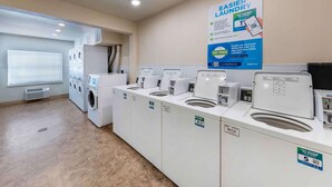 Un cuarto de lavandería con varias lavadoras y secadoras, un cartel que anuncia una aplicación móvil y un sistema de ventilación en la pared.
