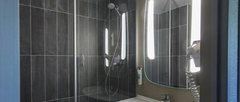A modern bathroom with a glass-enclosed shower, a white sink, and a large mirror.