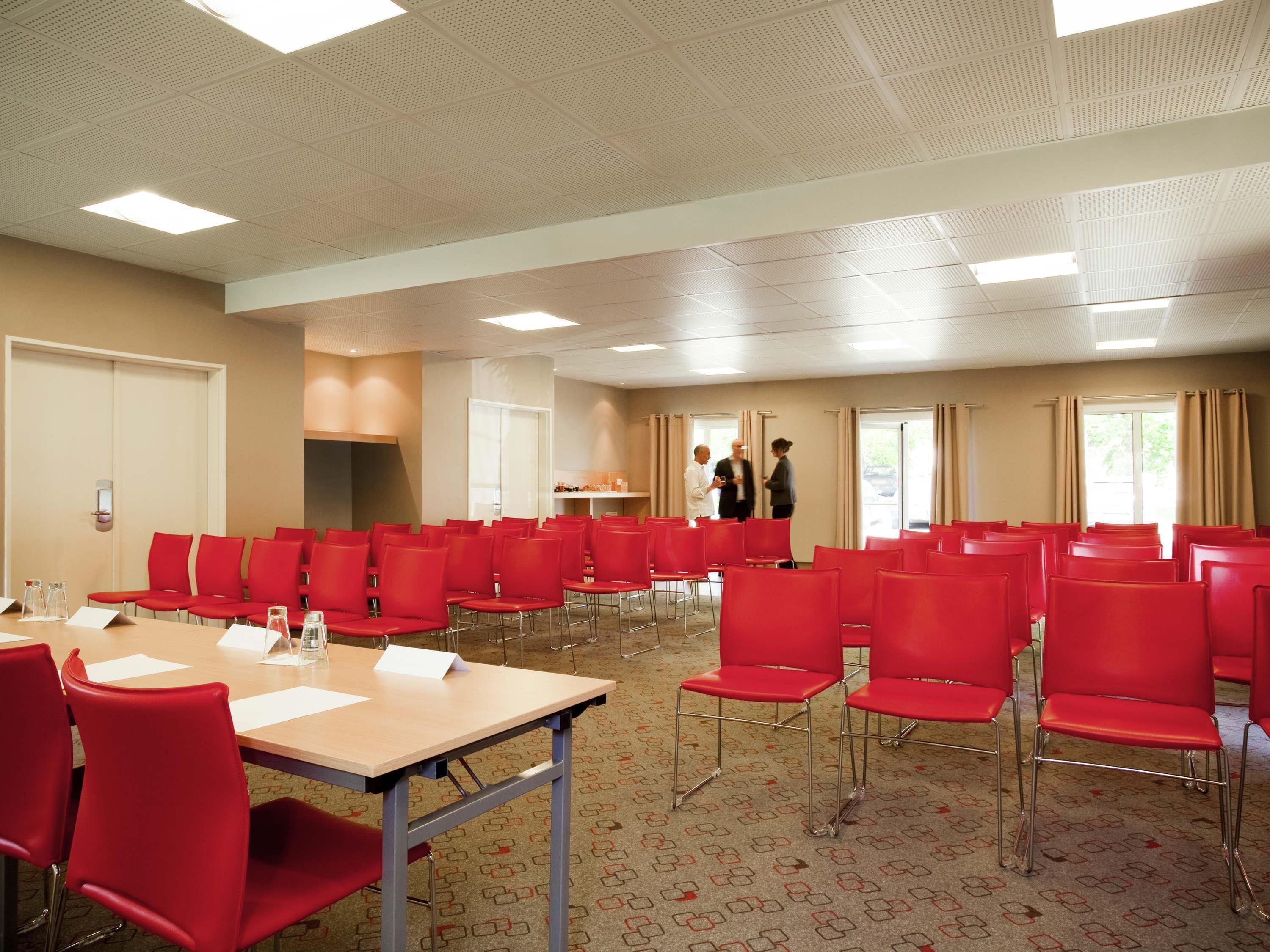 A conference room with red chairs, a long table, and a ceiling with recessed lighting.