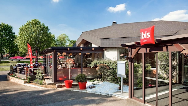 A modern hotel with a glass facade, outdoor seating area, and a red 'ibis Hotels' sign. - ibis Senlis (Senlis)