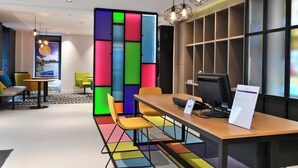 A modern office space with a colorful partition, a wooden desk with a computer, yellow chairs, and pendant lighting. - East Side Hotel Paris Gare de l’Est, a member of Radisson Individuals (Paris)
