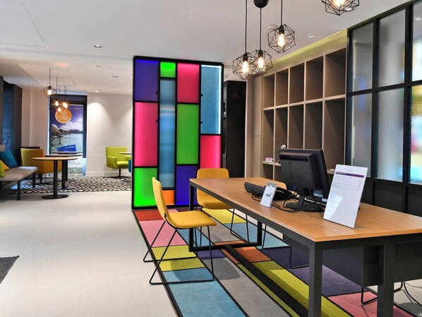 A modern office space with a colorful partition, a wooden desk with a computer, yellow chairs, and pendant lighting. - East Side Hotel Paris Gare de l’Est, a member of Radisson Individuals (Paris)