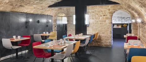 Un restaurante con paredes de piedra y asientos modernos. Las mesas están dispuestas en forma de U, y hay sillas de colores.