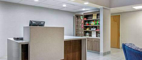 Zona de recepción con mostrador, computadora y estante con diversos artículos.