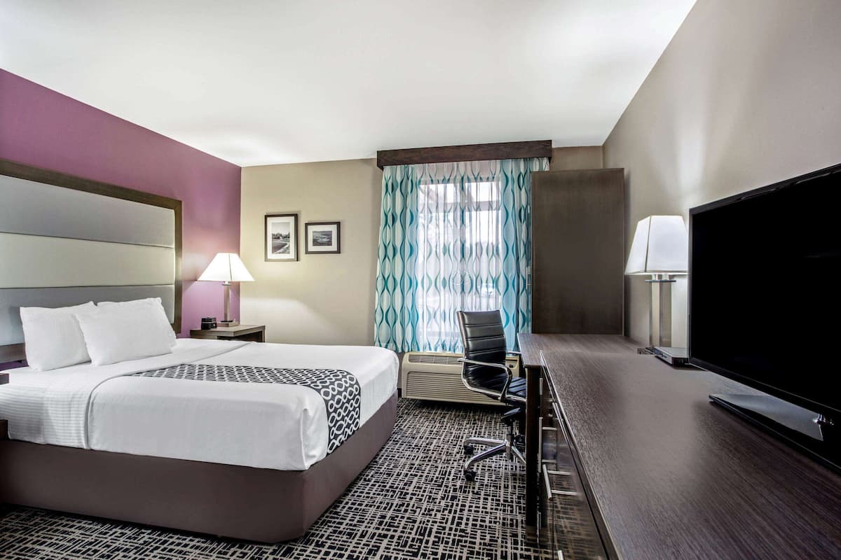 A hotel room with a bed, desk, chair, television, and curtains.