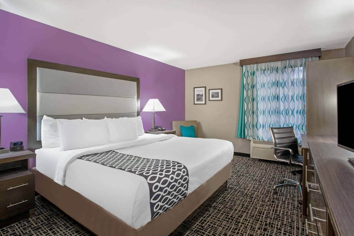 A hotel room with a large bed, a desk, a chair, a lamp, and a television.