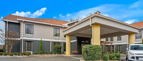 Un hotel con entrada cubierta, varios pisos y zona de estacionamiento.