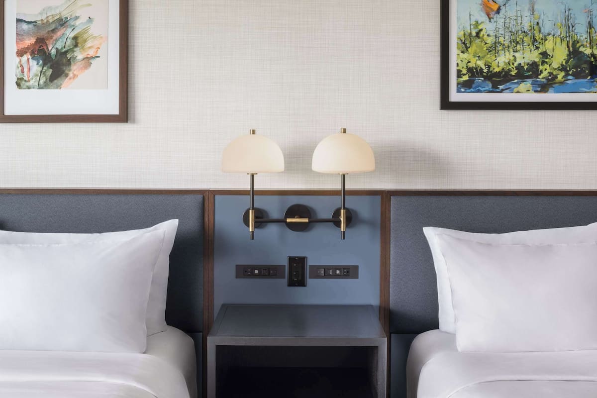 Une chambre d’hôtel avec deux lits, une table de chevet et des lampes fixées au mur.