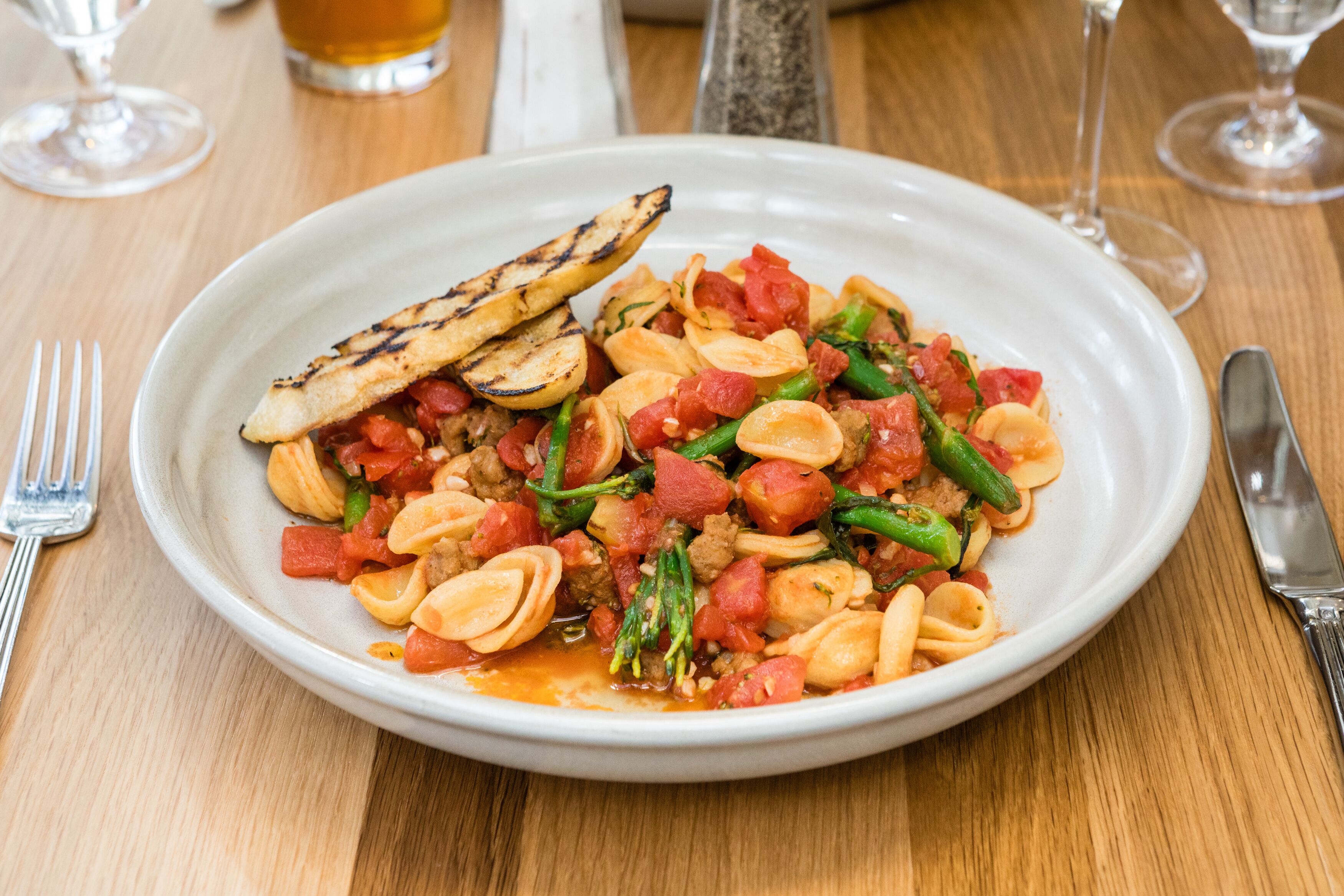 A plate of pasta with vegetables and grilled slices on a wooden table.