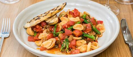A plate of pasta with vegetables and grilled slices on a wooden table.