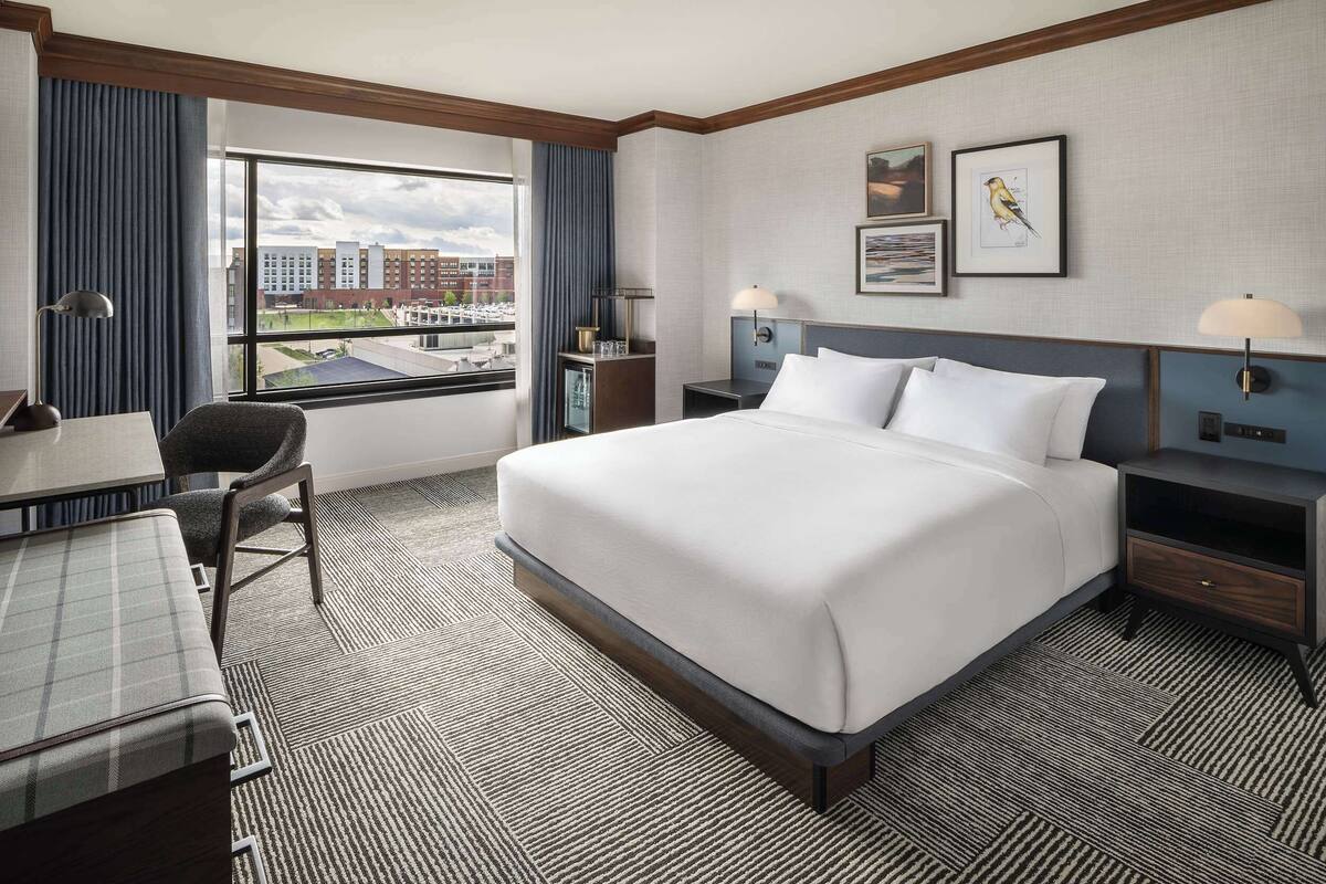 Une chambre d’hôtel avec un grand lit, un bureau et une chaise. Il y a une fenêtre donnant sur les bâtiments environnants.