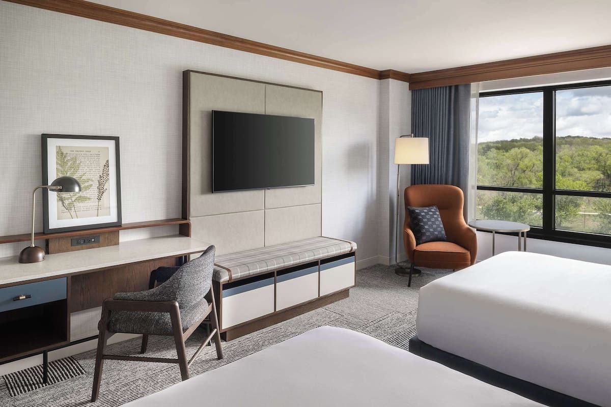Une chambre d’hôtel avec un lit, un bureau et une chaise, une télévision et une fenêtre donnant sur des arbres.
