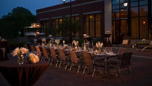 An outdoor dining area with tables set for a meal, surrounded by brick buildings and a street lamp.