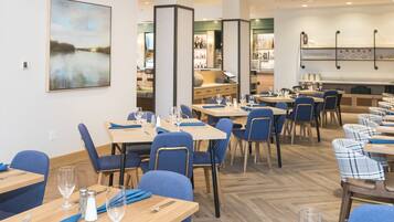 A restaurant with multiple tables, blue chairs, and a bar area in the background.