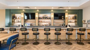 A bar area with wooden flooring, bar stools, and a counter stocked with various bottles and glasses.