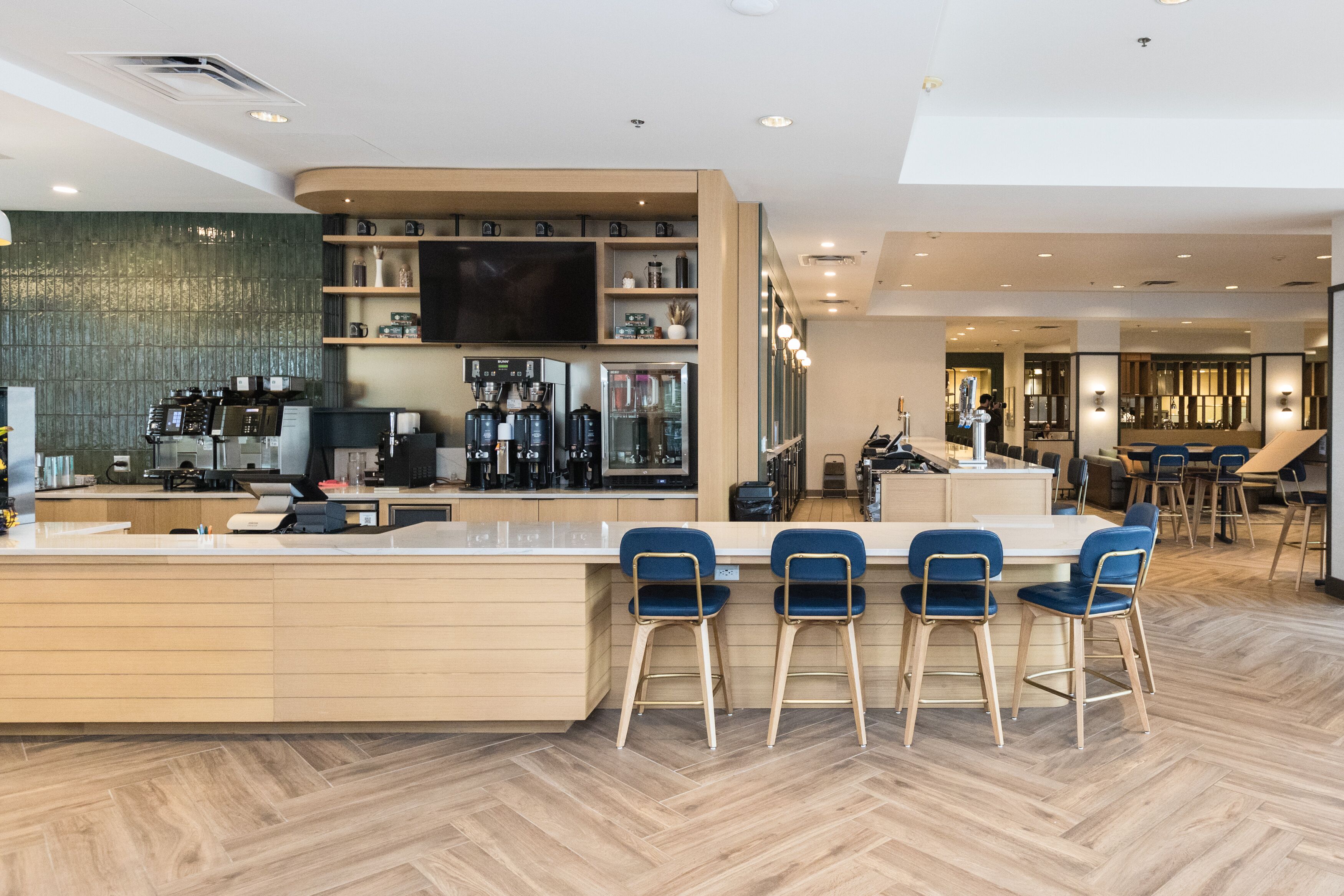 Un área de bar moderna con una barra larga, taburetes y una pantalla de televisión.