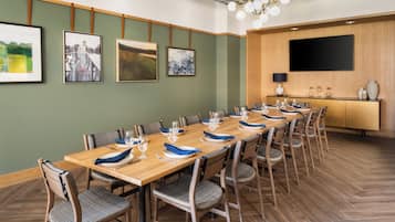 Une salle de conférence avec une longue table en bois, des chaises et un téléviseur à écran plat fixé au mur.