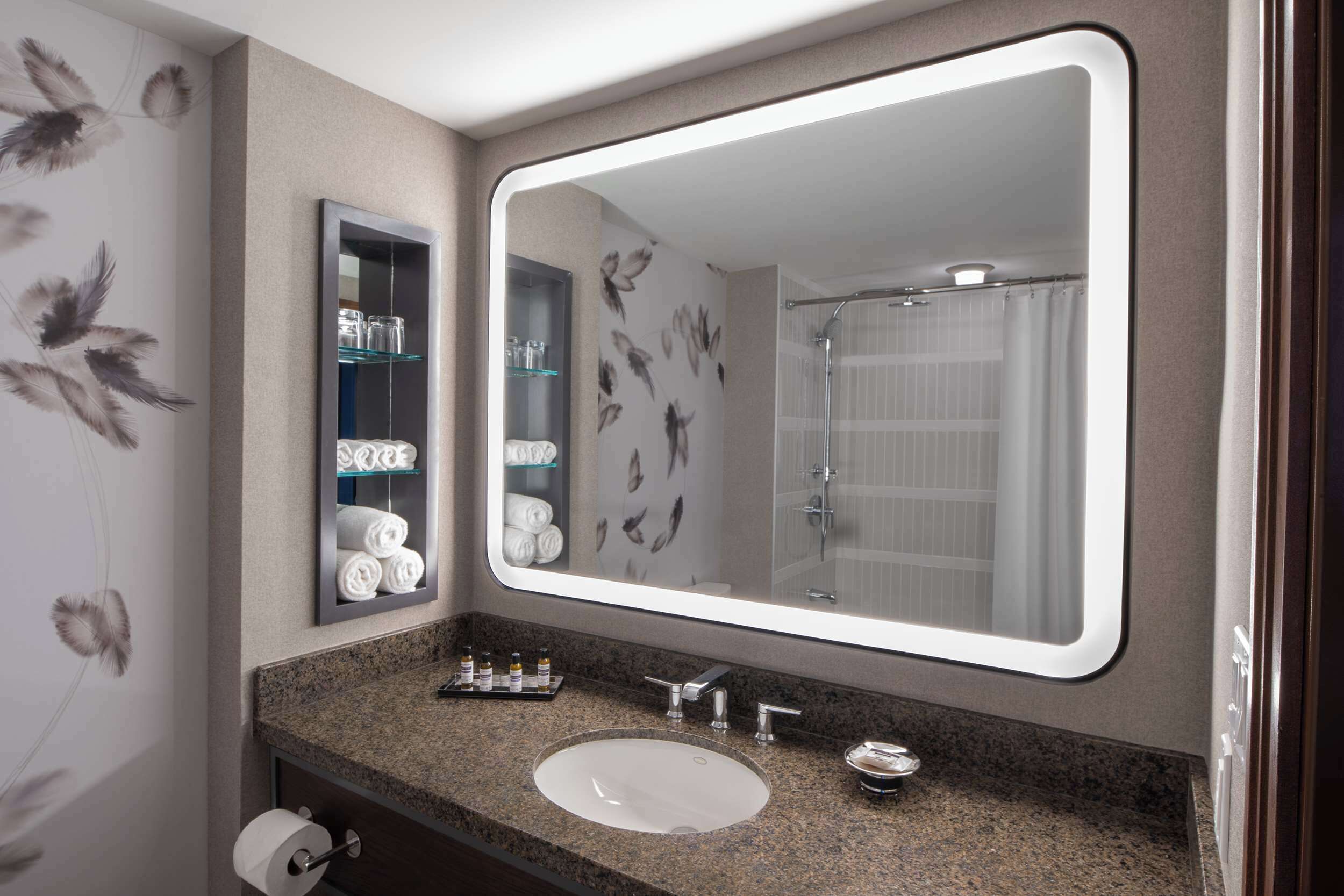 A bathroom with a large mirror, granite countertop, sink, and towel rack.