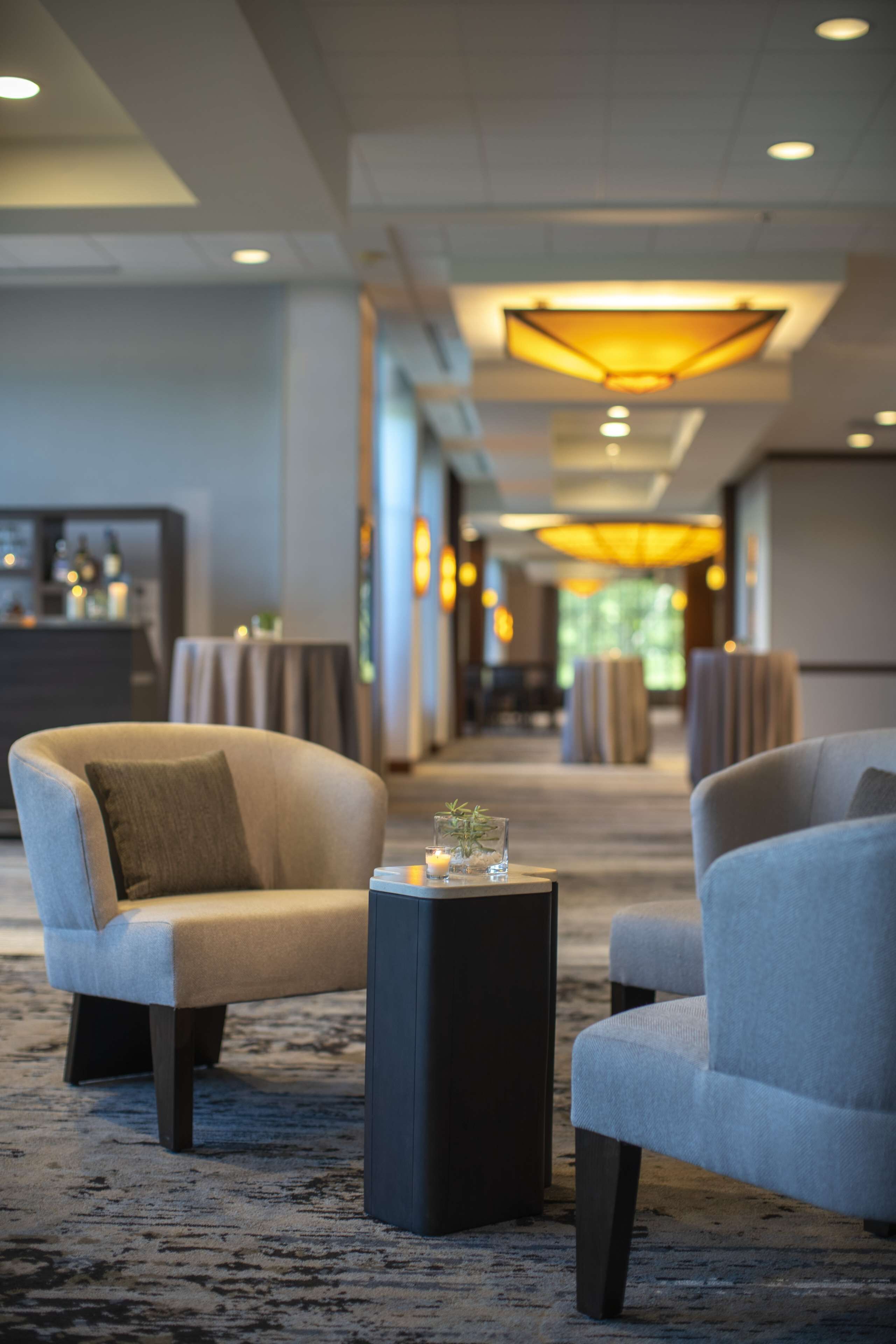 A hotel lobby with two armchairs, a small table with a candle, and a reception desk in the background.