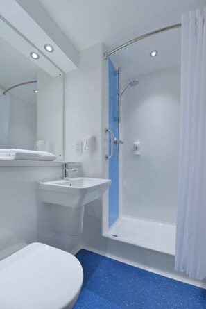 A modern bathroom with a white toilet, a sink, a shower with a glass door, and a blue speckled floor. - Travelodge Norwich Central (Norwich)