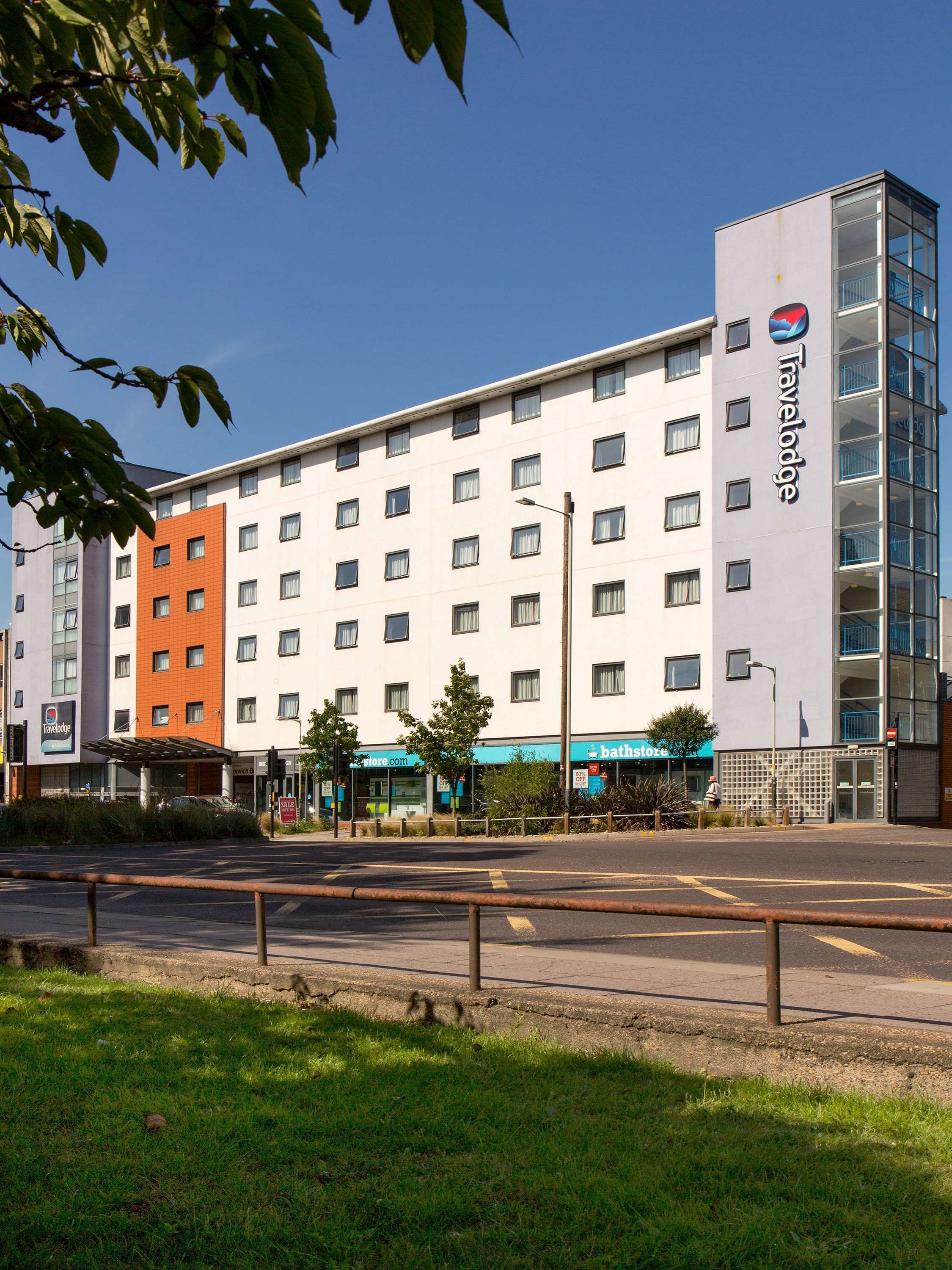 A Travelodge hotel with a modern design, featuring a mix of white and orange facades, multiple windows, and a prominent Travelodge sign.