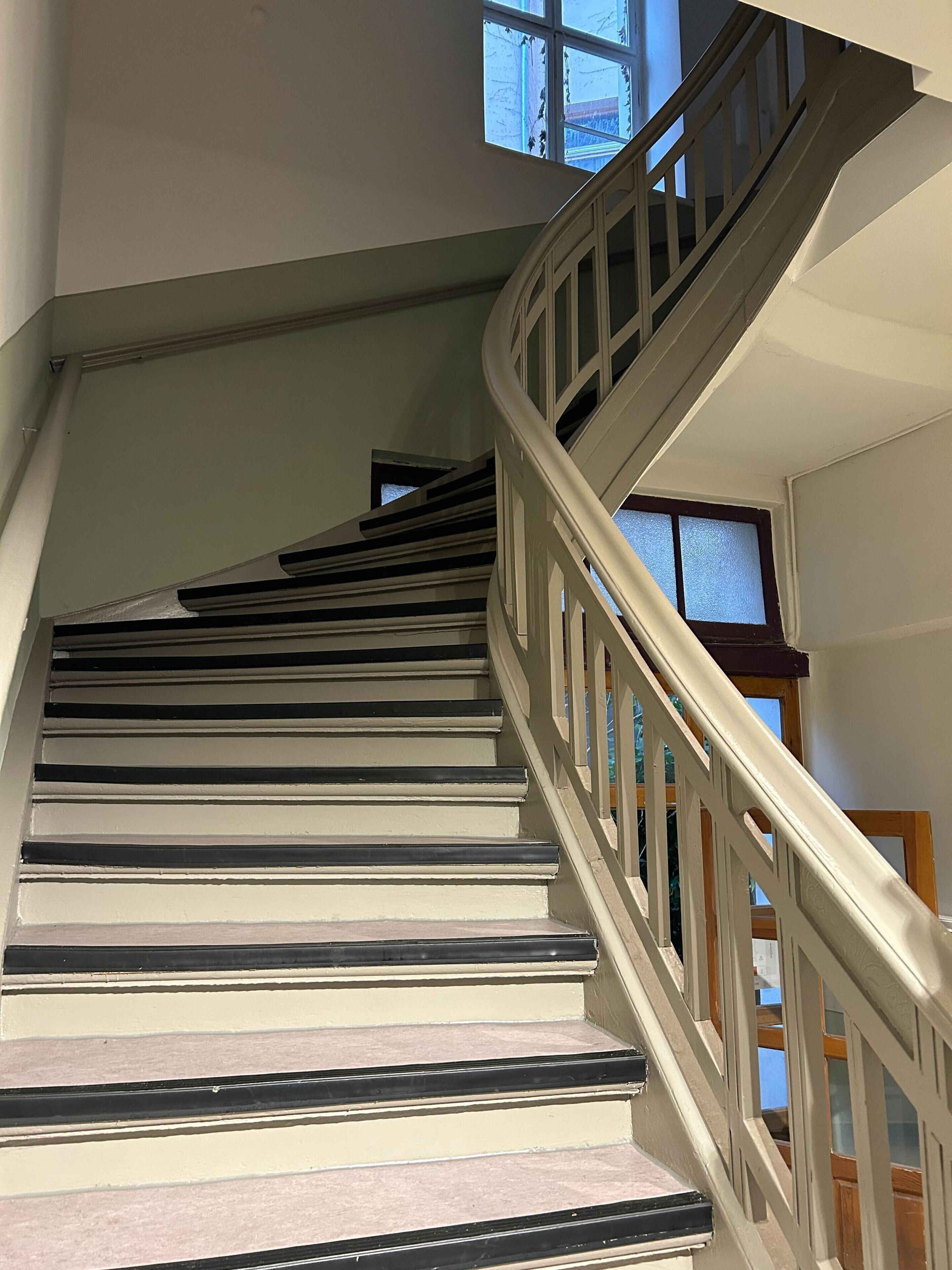 Una escalera con peldaños blancos y bordes negros que conduce a una plataforma con una ventana.