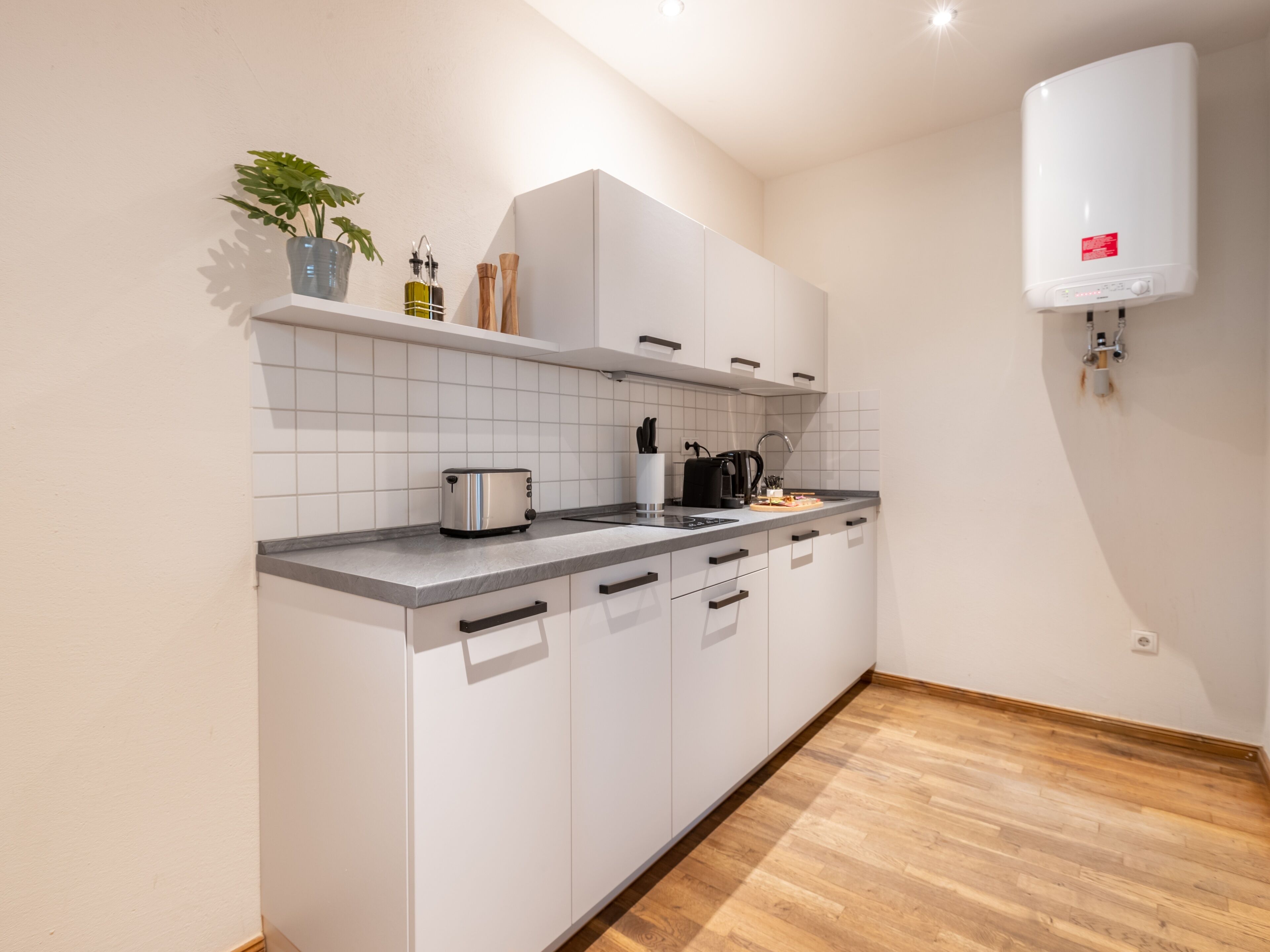 Une cuisine moderne avec des meubles blancs, un plan de travail gris et un plancher en bois.