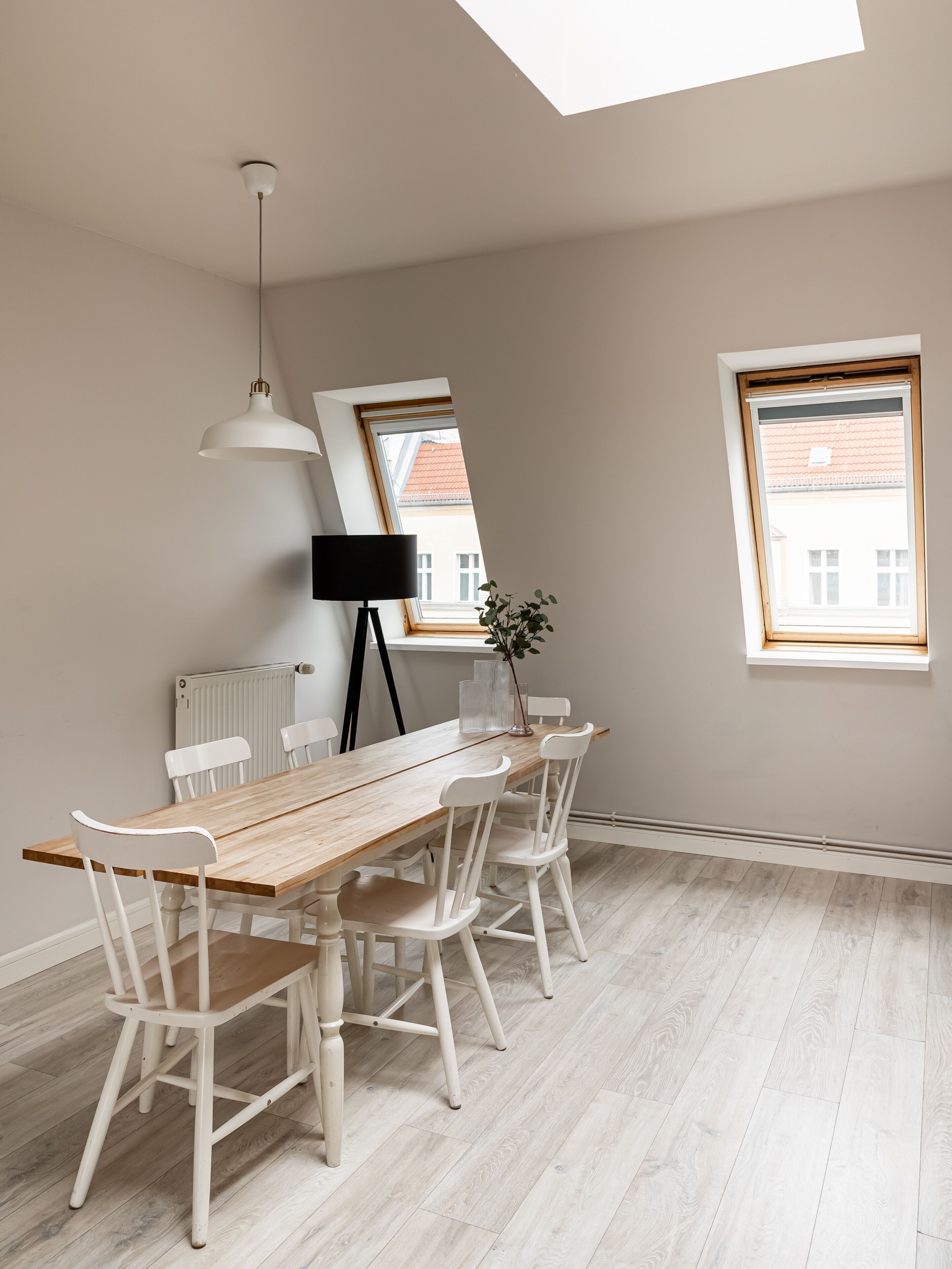 Un comedor con una mesa de madera y sillas blancas, una lámpara de pie negra y un radiador.