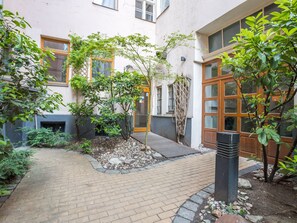 Ein Innenhof mit Pflasterweg, Holztür und kleinem Gartenbereich mit Pflanzen und Steinen.