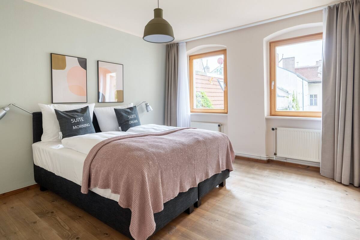 Un dormitorio con cama, lámpara colgante, ventana y radiador.