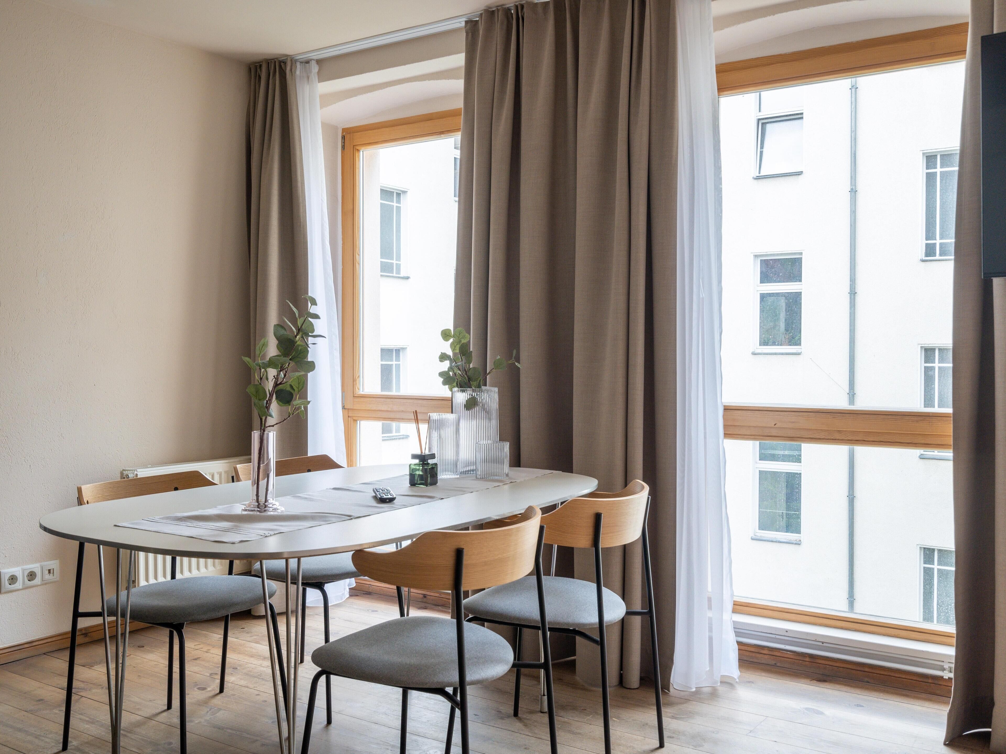 Een eetruimte met een ronde tafel, zes stoelen en een raam met gordijnen.