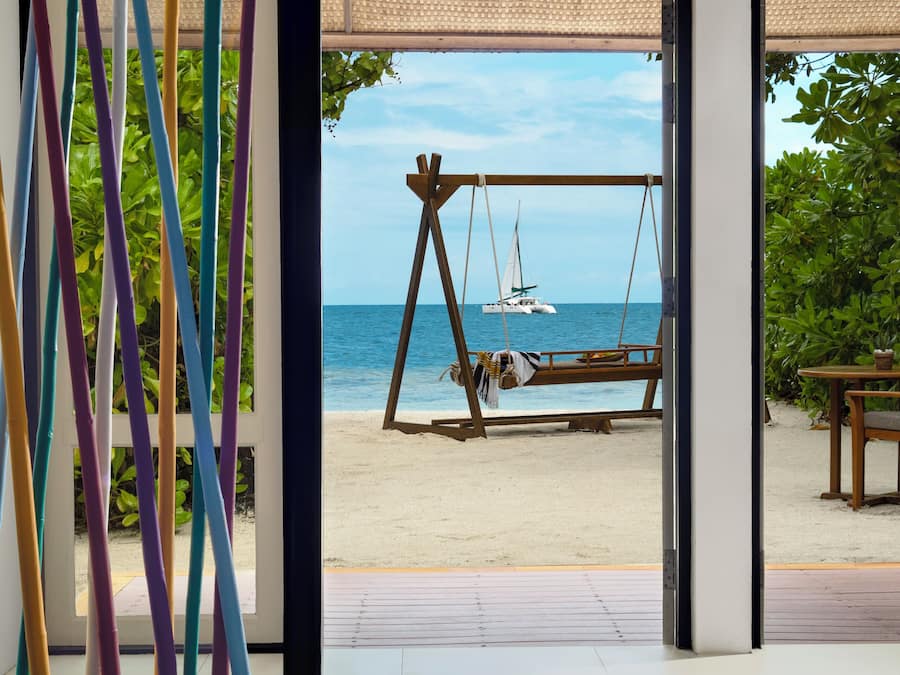 A beach view from a room with a swing set and a boat in the distance.