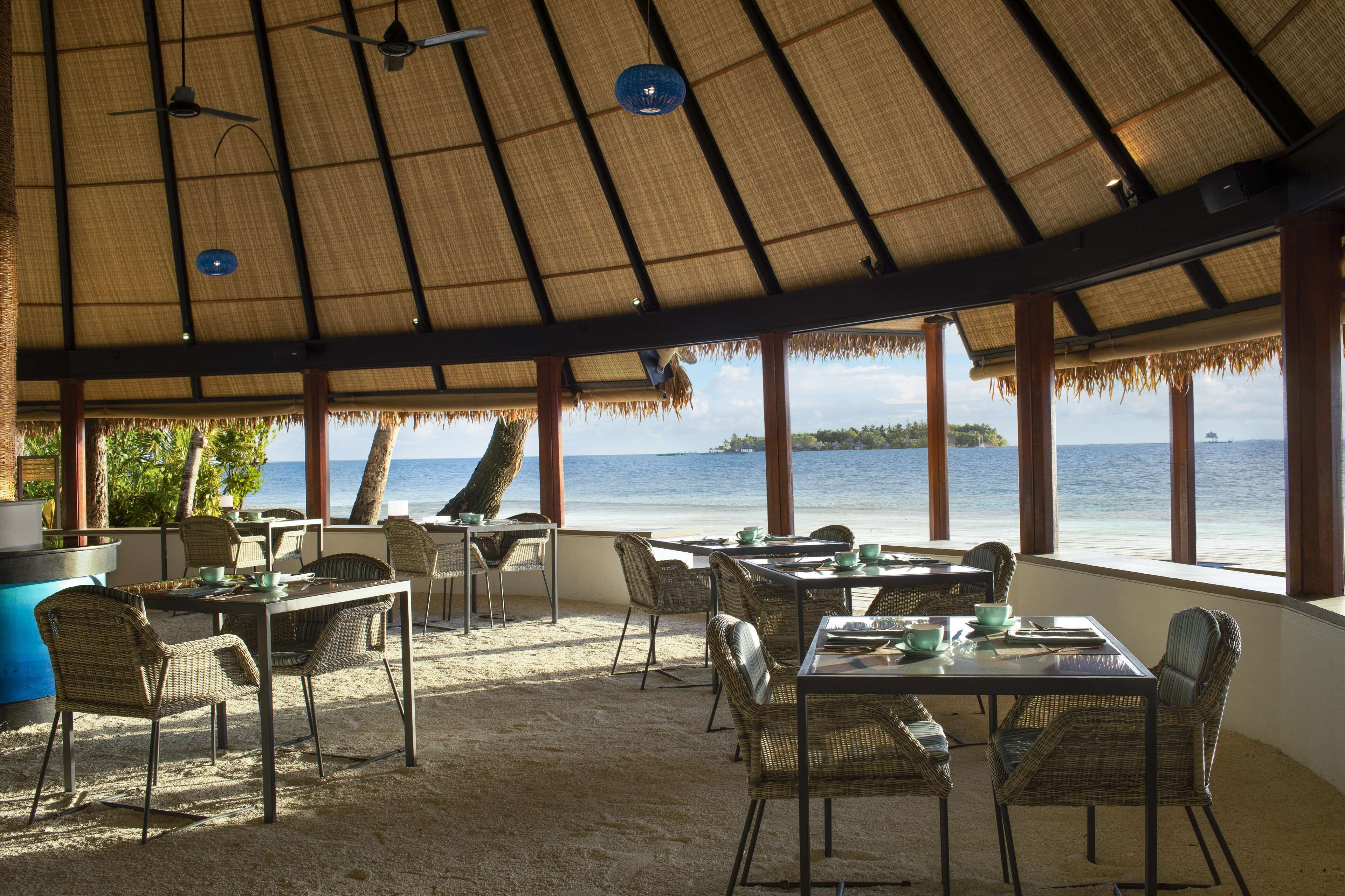 An outdoor dining area with thatched roofs, wicker furniture, and a view of the sea.