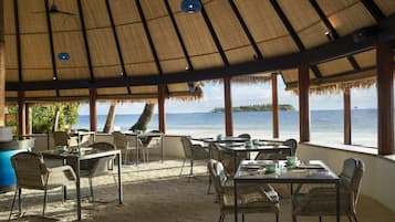 An outdoor dining area with thatched roofs, wicker furniture, and a view of the sea.