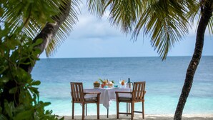A table set on a sandy beach with a view of the ocean, surrounded by palm trees. - Dhawa Ihuru, part of Banyan Group – All inclusive with Free Transfer (Ihuru)