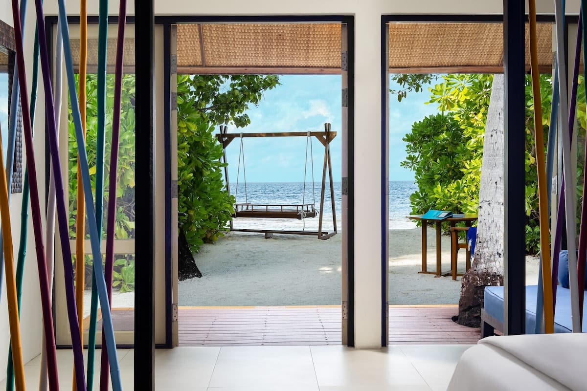 A room with a swing set on a beach view, a wooden table, and a blue sofa.