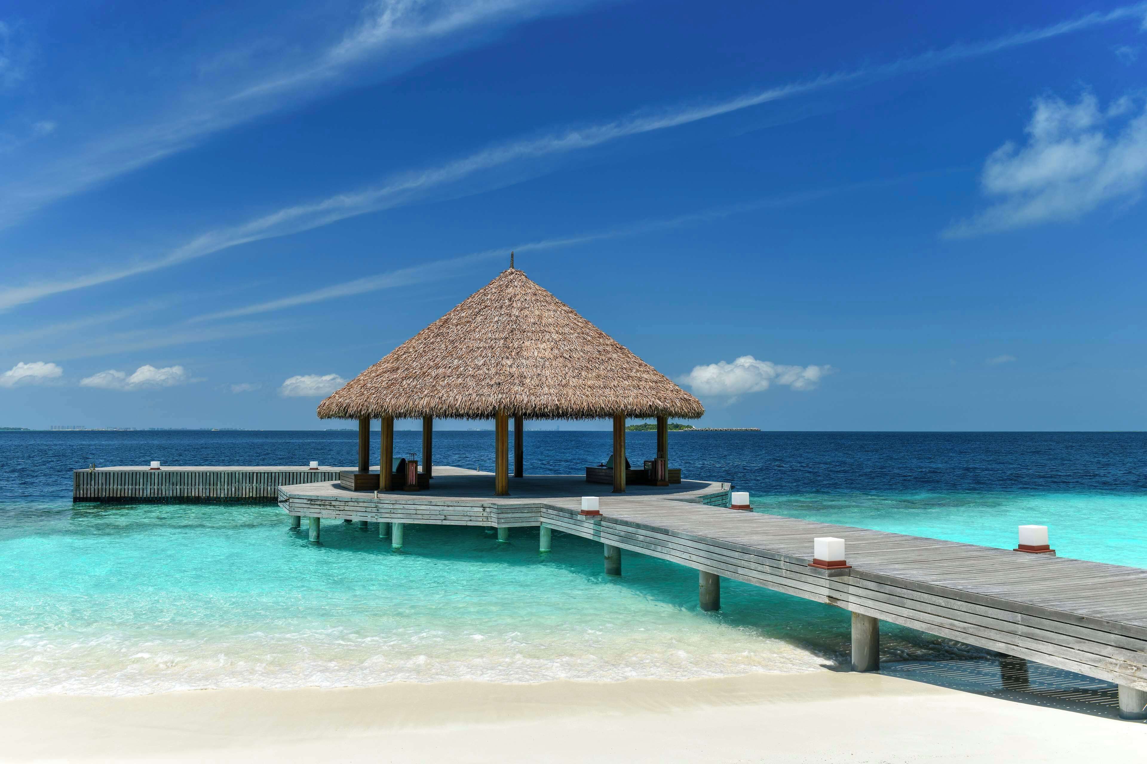 A wooden pier leading to a thatched-roof structure over turquoise waters.