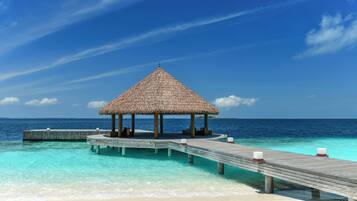 A wooden pier leading to a thatched-roof structure over turquoise waters.