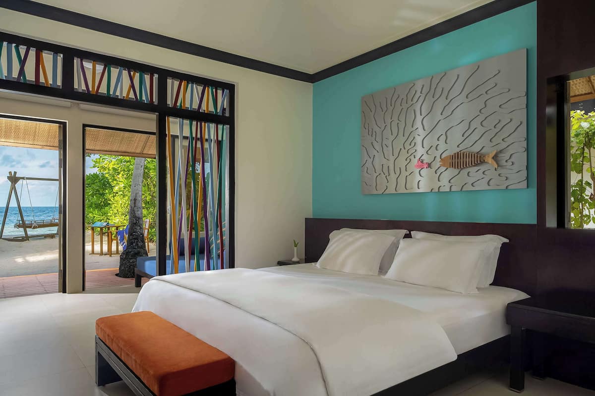 A bedroom with a bed, a bench, and a view of a beach through a glass door.
