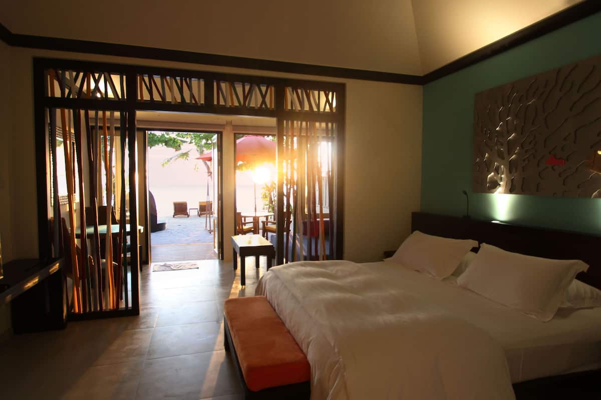 A hotel room with a large bed, a wooden partition, and a view of an outdoor seating area.