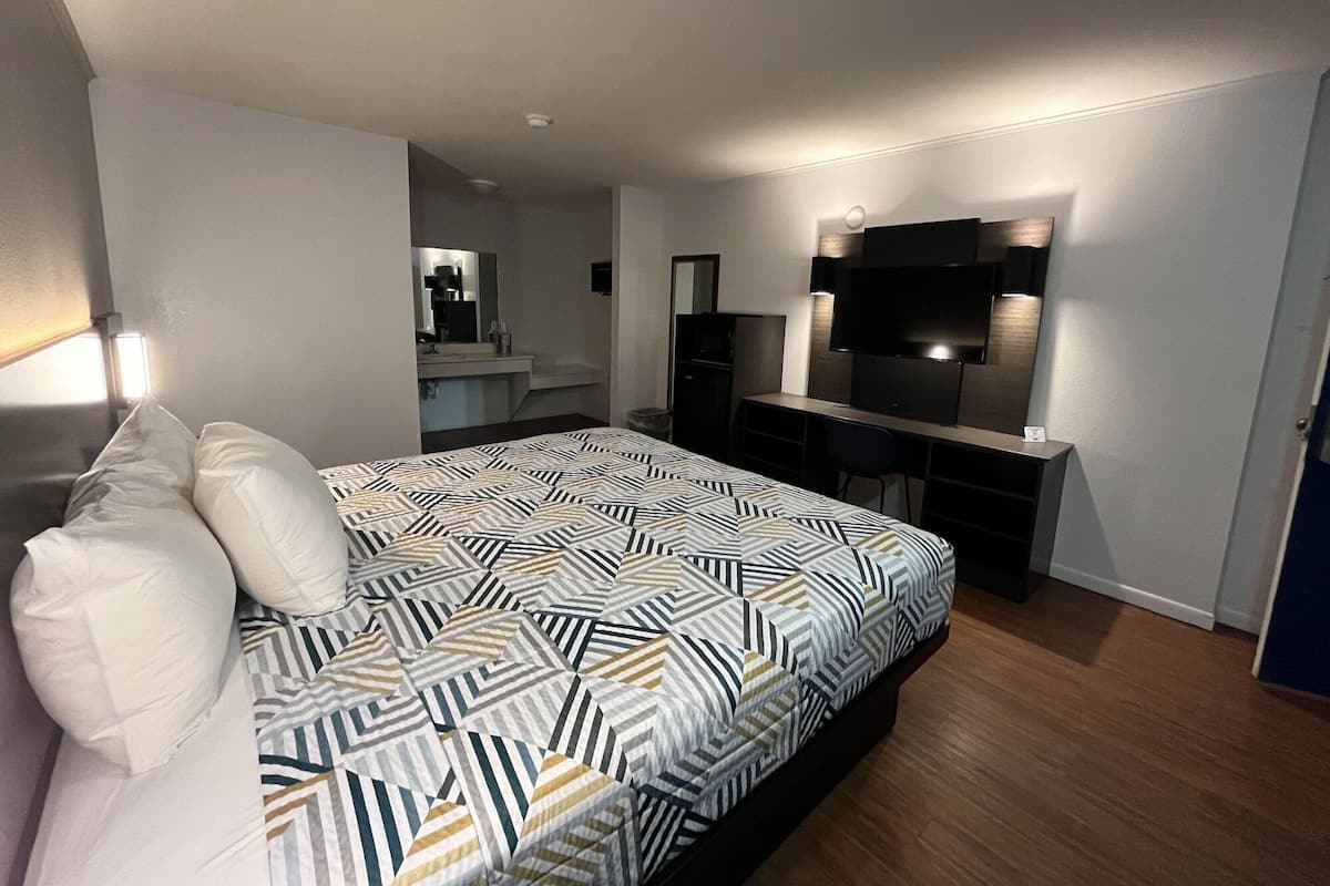 A modern hotel room with a large bed, a desk, a flat-screen TV, and a mirror.