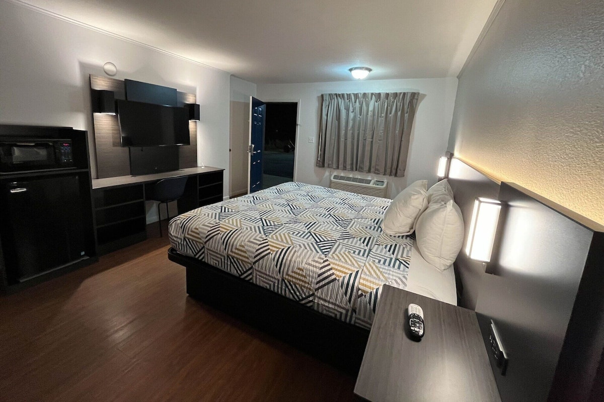 A hotel room with a bed, a desk with a TV, a microwave, and a wardrobe.