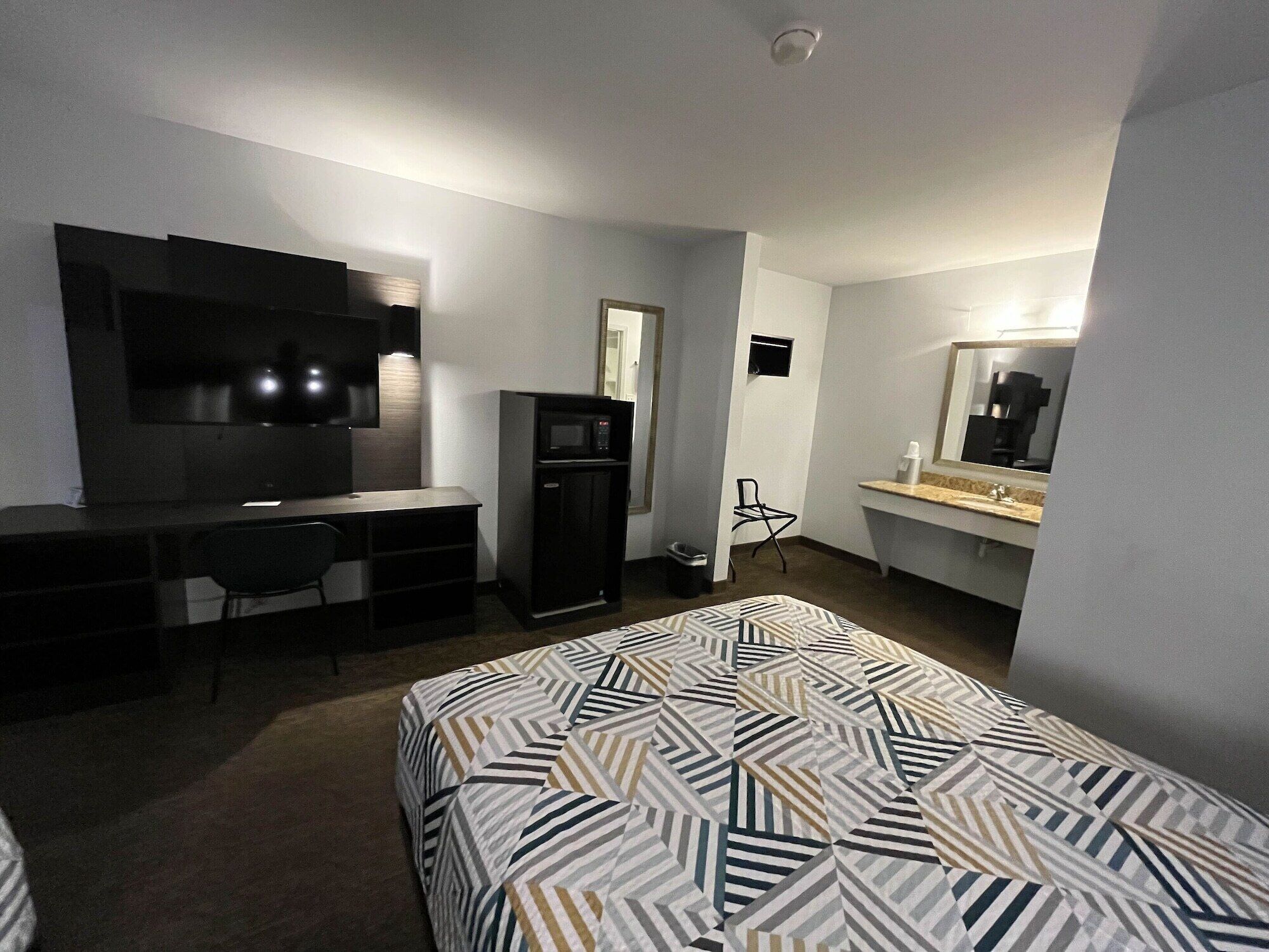 Une chambre d’hôtel équipée d’un lit, d’un bureau, d’une télévision, d’un four à micro-ondes, d’une chaise et d’une petite salle de bain.