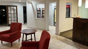 A hotel lobby with red armchairs, a round wooden table, a minibar, and a reception desk. - Motel 6 Junction, Texas - Llano River (Junction)