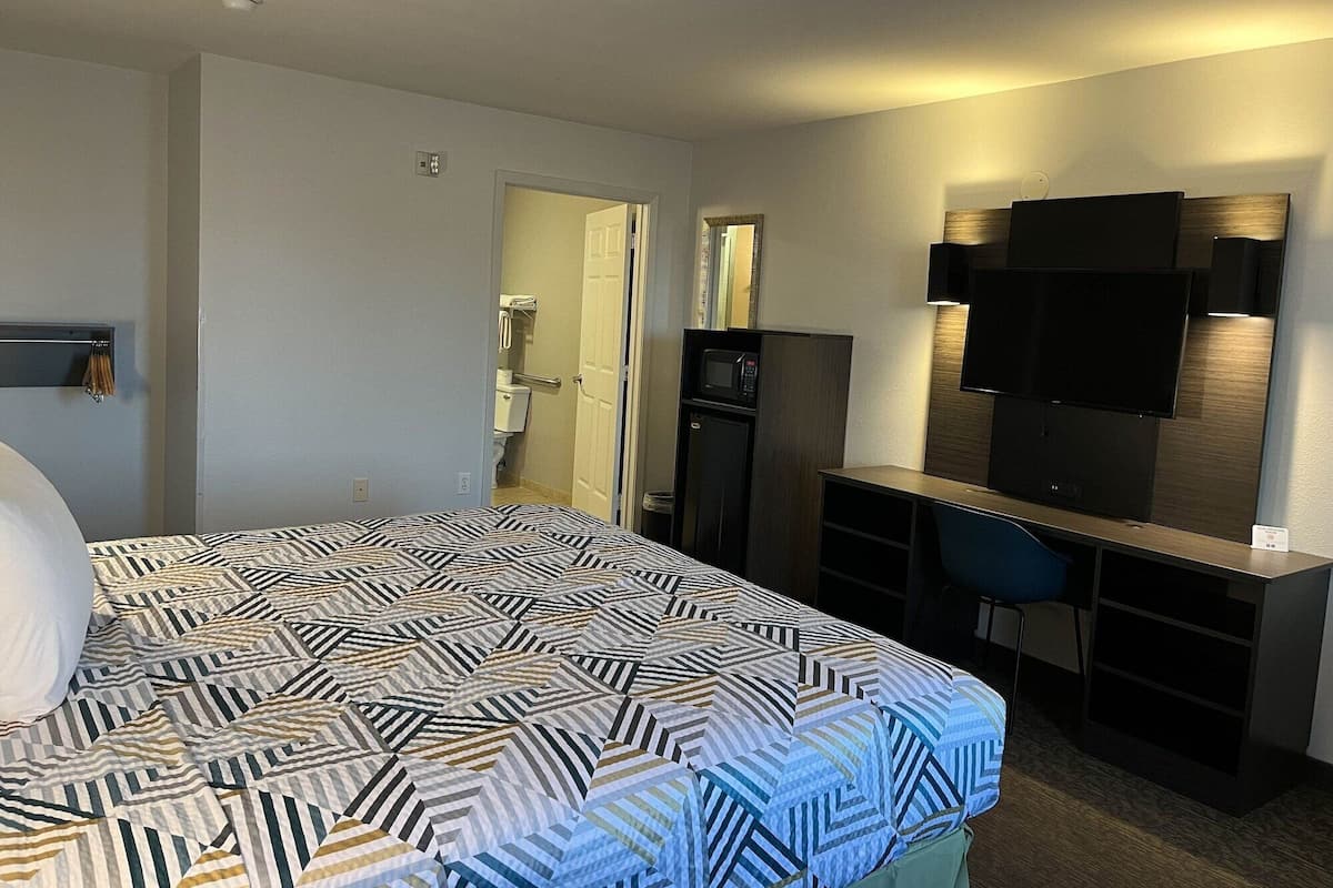 A hotel room with a bed, a desk with a chair, a TV, and a microwave.