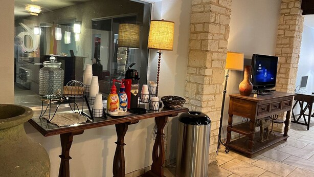 A kitchen area with a coffee station, a trash can, a TV, and a stone wall. - Motel 6 Junction, Texas - Llano River (Junction)