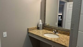 A bathroom with a granite countertop sink, a mirror, and a towel dispenser.