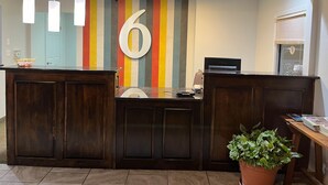 A reception desk with a large '6' sign, a potted plant, and a window with blinds. - Motel 6 Junction, Texas - Llano River (Junction)
