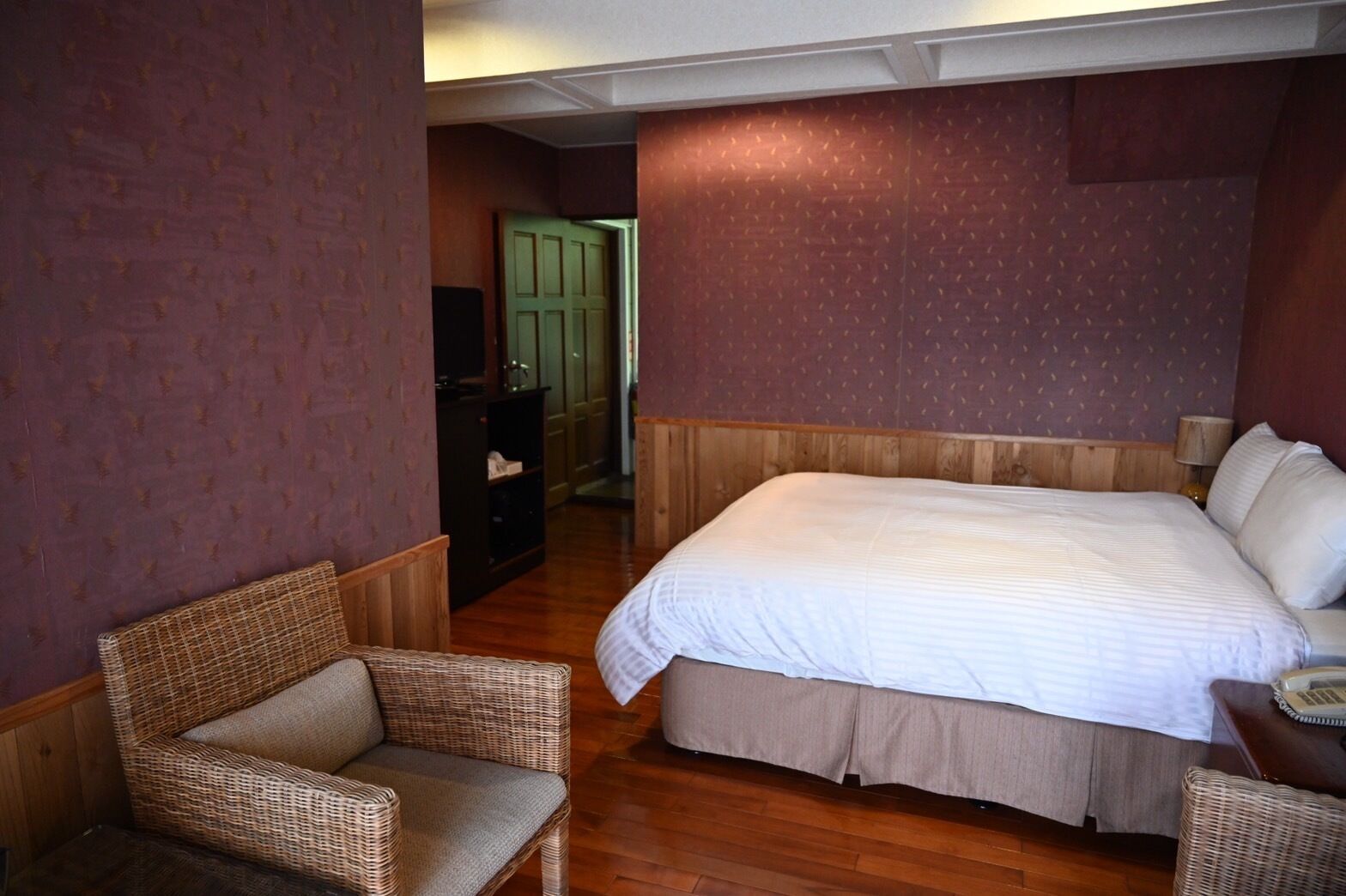 Un dormitorio con una cama grande, una silla de mimbre y un armario de madera.